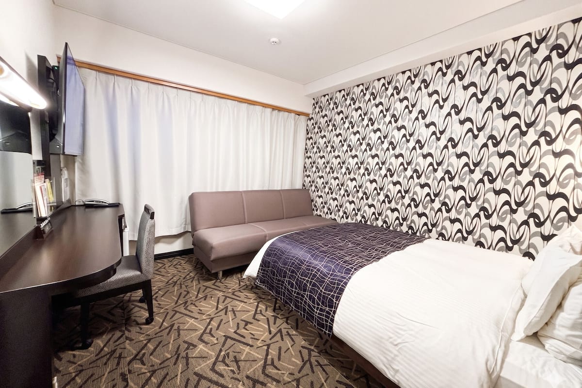 Habitación de hotel con una cama, un sofá, un escritorio y una televisión.