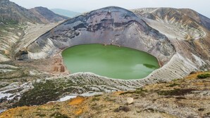 Ein großer, grüner Krater, umgeben von zerklüftetem, felsigem Gelände.