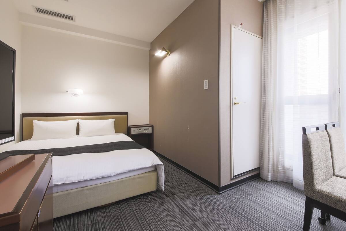Una habitación de hotel con cama, mesita de noche, lámpara y una silla.