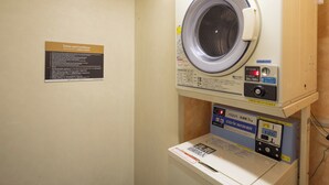 Ein Waschraum mit einer Waschmaschine mit Frontlader und einem Trockner. Ein Schild an der Wand zeigt Nutzungsbedingungen.