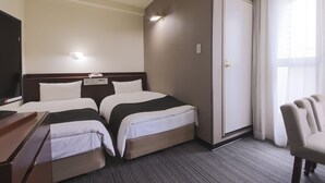 Ein Hotelzimmer mit zwei Betten, einem Schreibtisch, einem Sessel, einem Fernseher und einem Fenster mit Vorhängen.