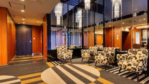 Un vestíbulo de hotel con diseño moderno, que presenta una zona de estar con sillas estampadas con motivos florales, una alfombra con diseño y una gran araña.