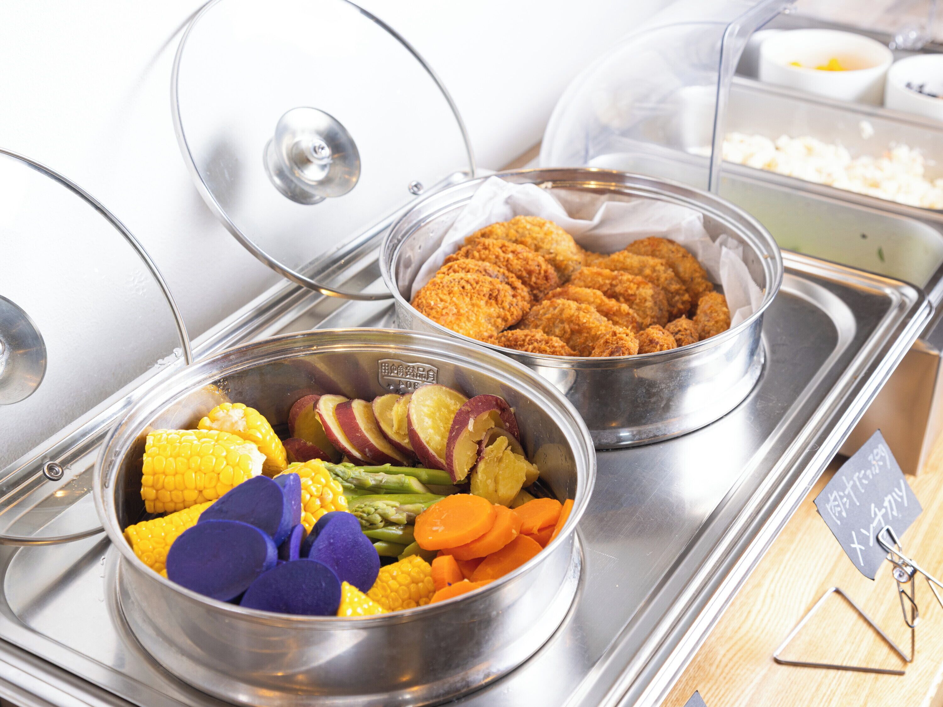 A buffet with various food items including corn, carrots, and a dish with a crispy coating.
