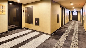 Pasillo de hotel con piso alfombrado, un ascensor empotrado en la pared y puertas que dan a las habitaciones.