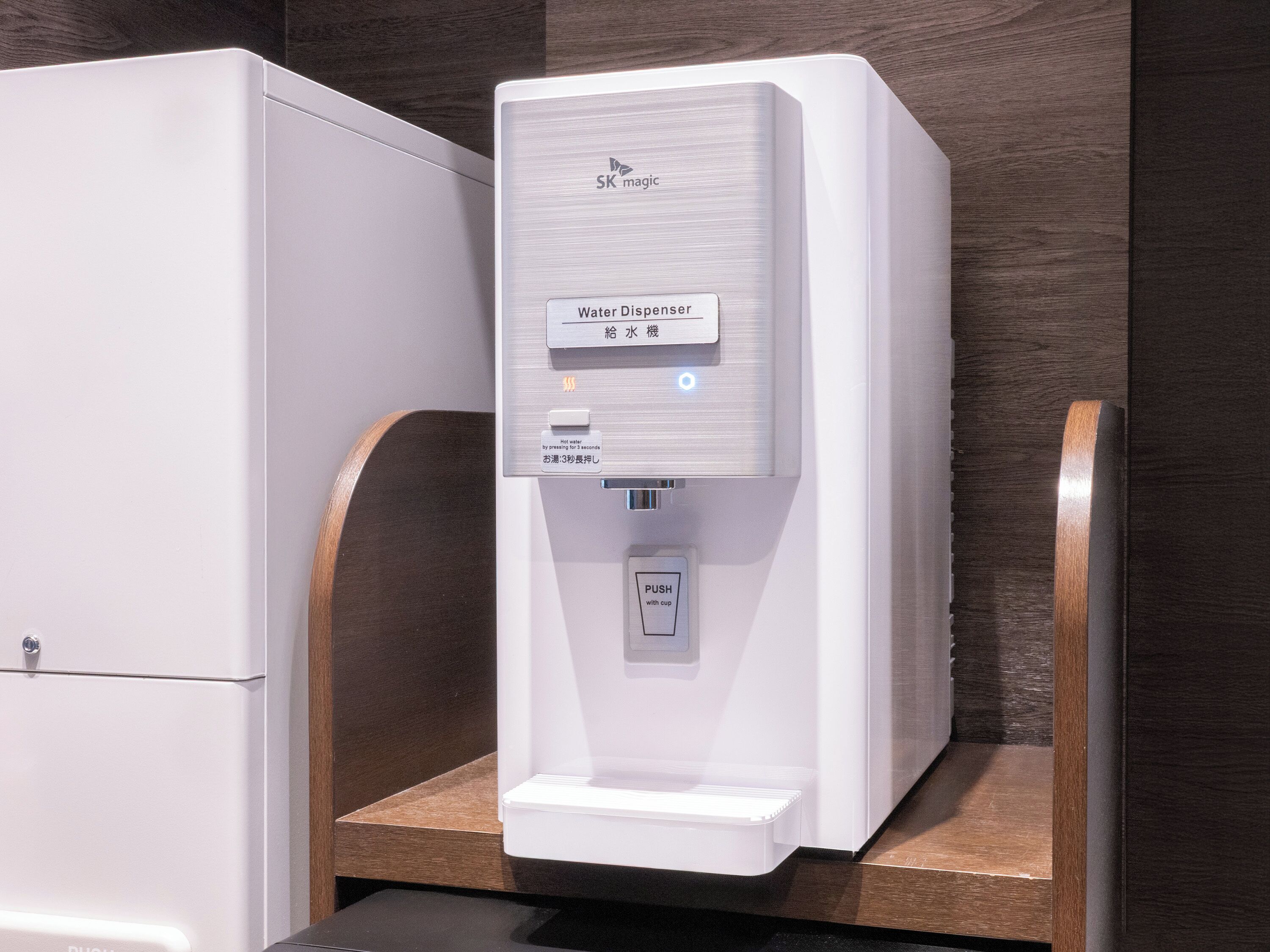A water dispenser with a push button, a hot water button, and a label in two languages.