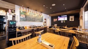 Interior de restaurante con mesas y sillas de madera, una máquina de café y un menú en una pizarra.