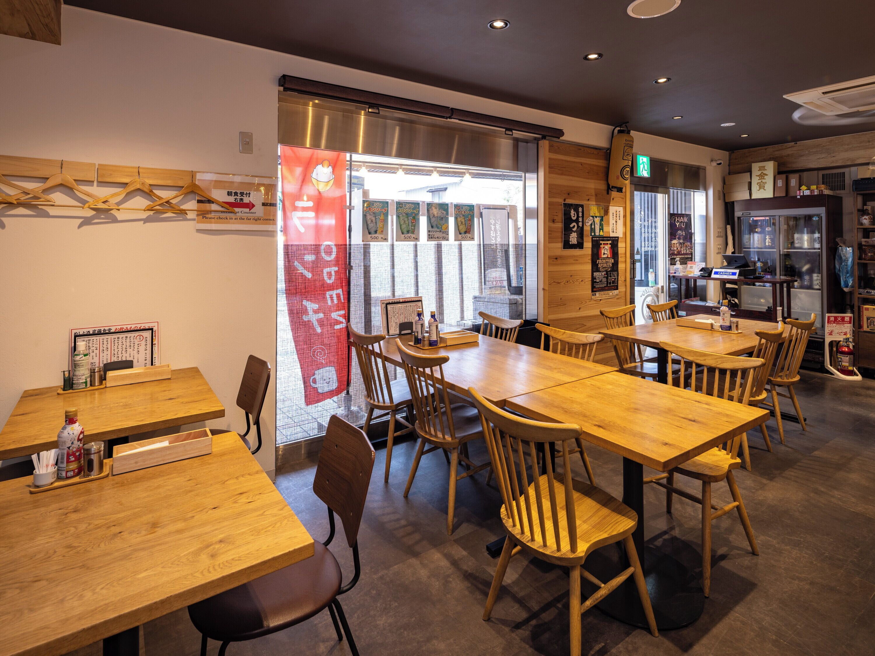 A restaurant interior with wooden tables and chairs, a counter with a menu, and a view through a glass door.
