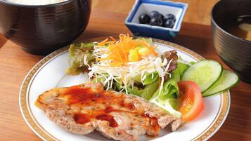 A plate with grilled chicken, salad, and vegetables on a table with a bowl of rice and a bowl of soup.