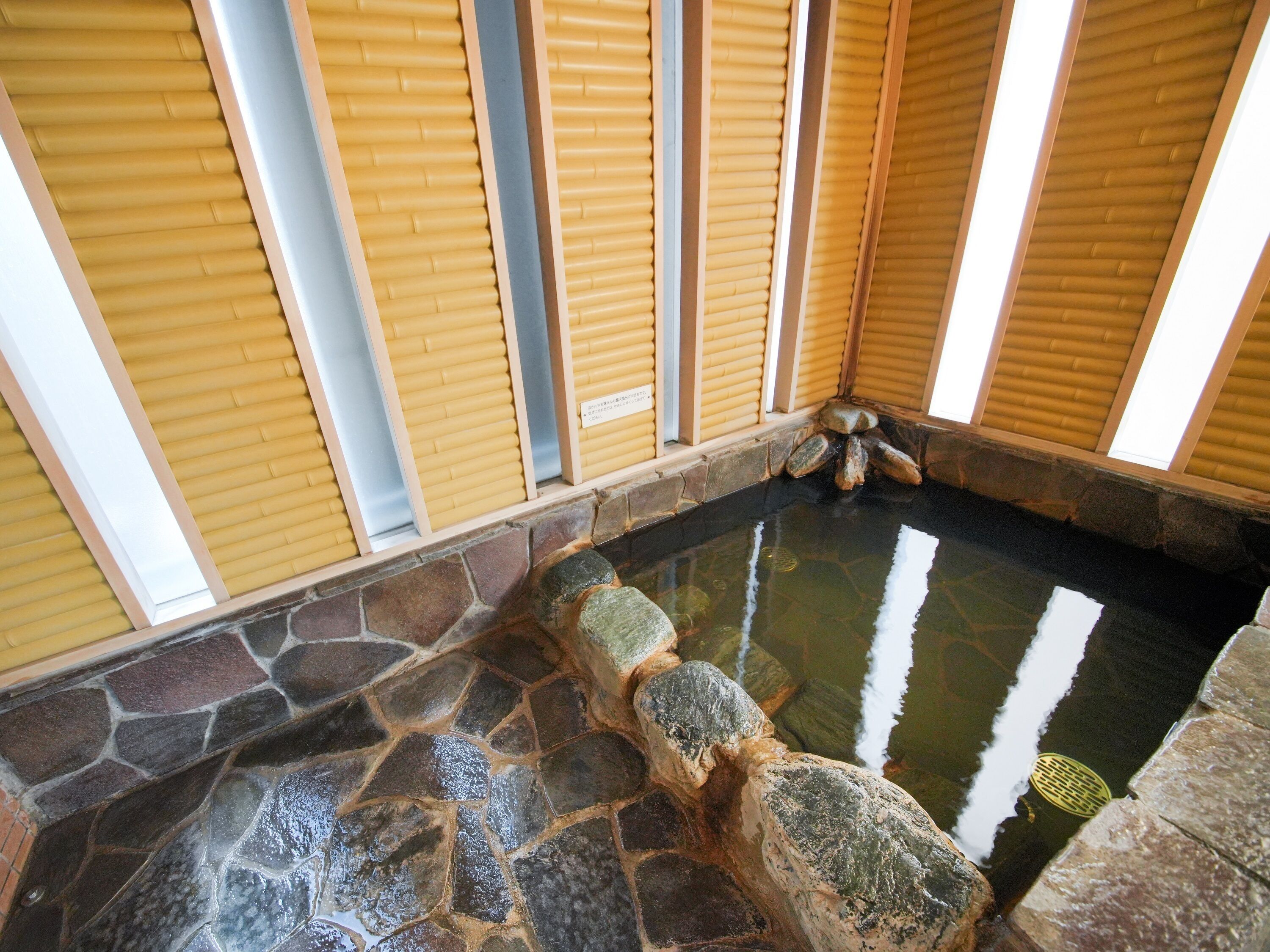 A stone-tiled hot spring area with wooden sliding doors and a stone wall.