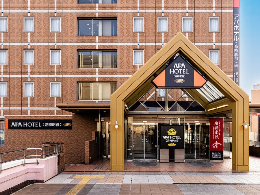Entrada del APA HOTEL con un diseño moderno, que incluye una estructura de techo triangular distintiva y un cartel.