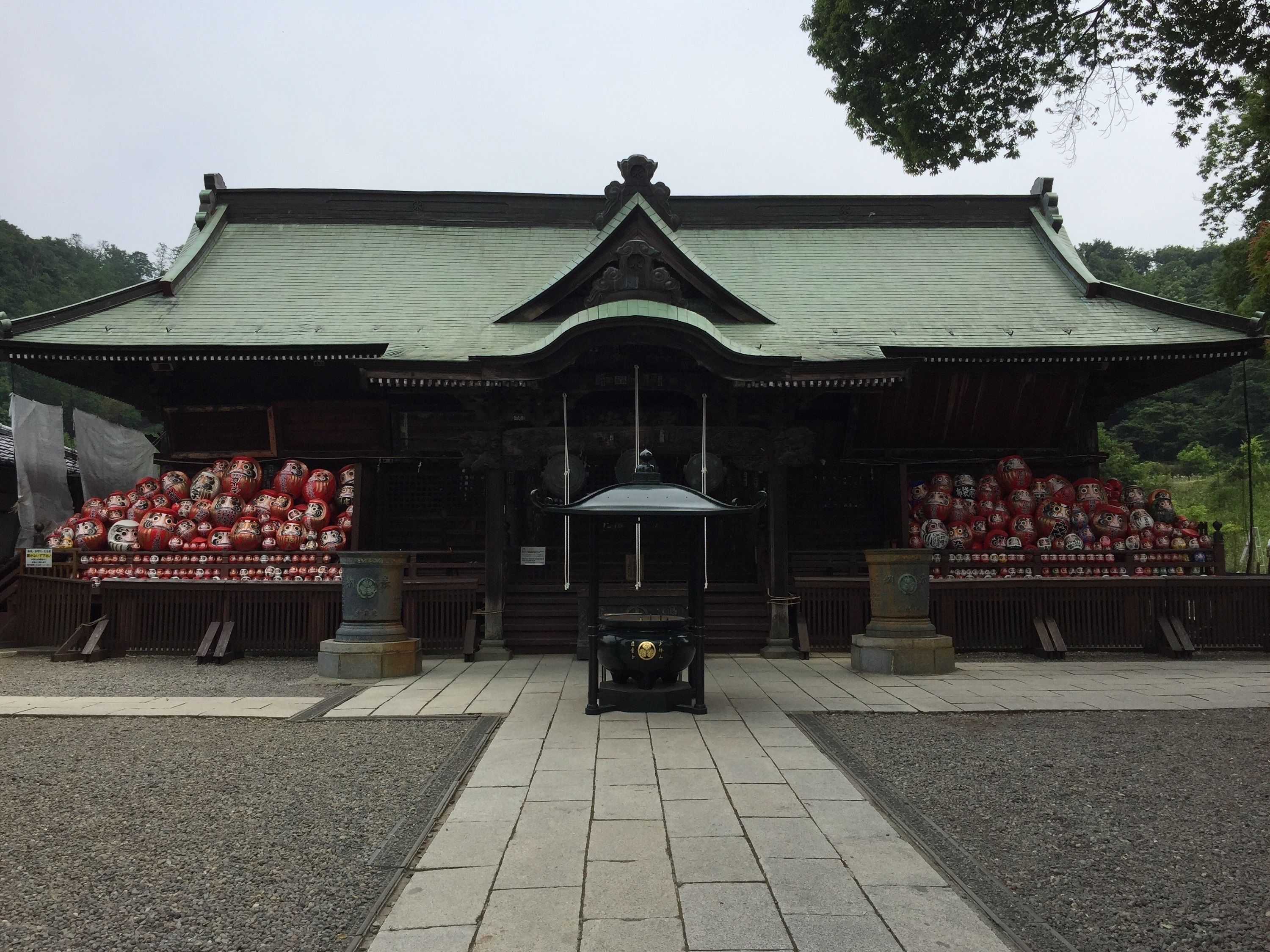 A traditional Japanese building with a green roof and wooden structure. In front, there are two displays of red and white dolls.