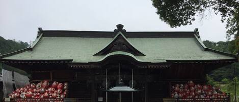 Edificio japonés tradicional con tejado verde y estructura de madera. En primer plano, se exhiben dos figuras de muñecas rojas y blancas.