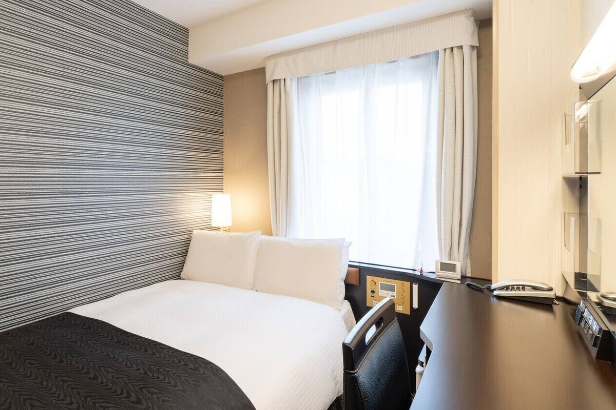 Ein Hotelzimmer mit Bett, Nachttisch, Lampe und einem Fenster mit Vorhängen.