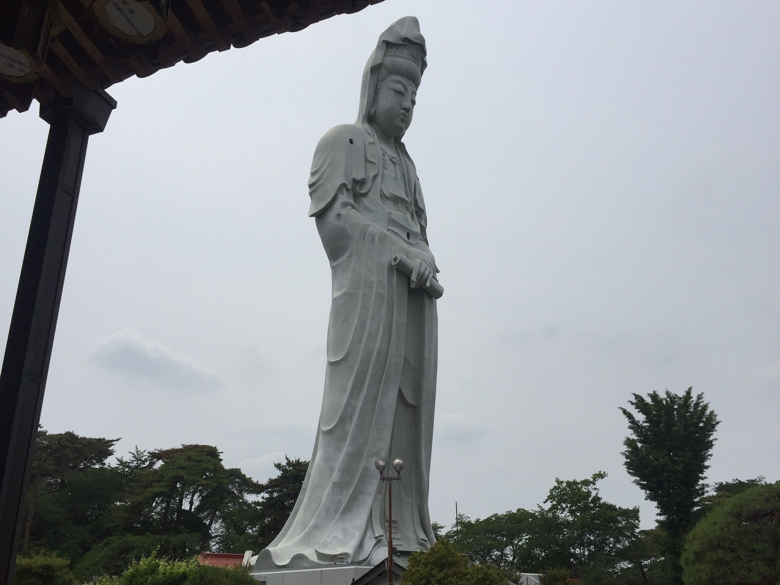 A large statue of a figure in traditional attire, standing under a covered structure.