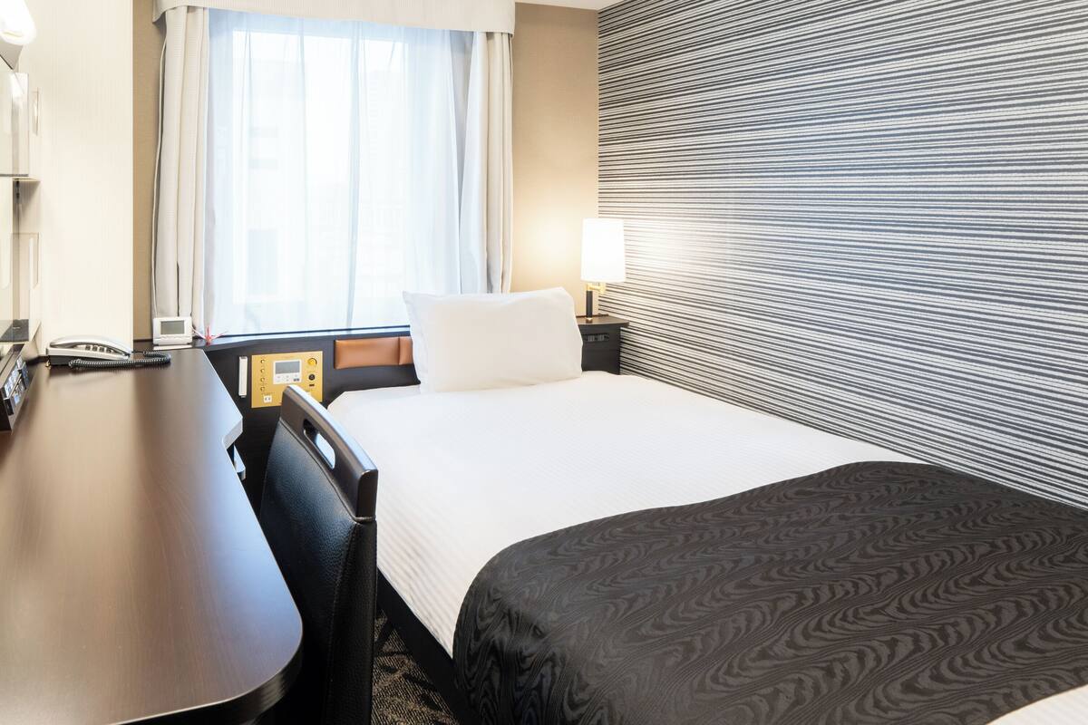 Une chambre d’hôtel avec un lit, une table de chevet, une lampe et une fenêtre avec des rideaux.