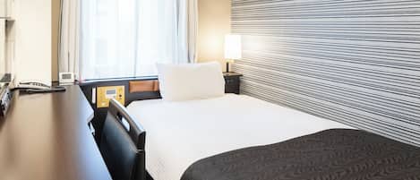 A hotel room with a bed, bedside table, lamp, and a window with curtains.