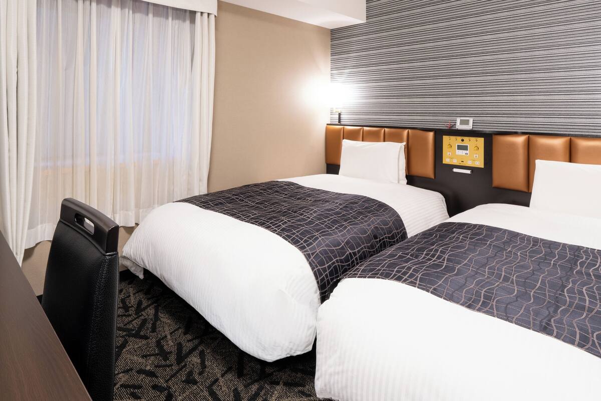 Une chambre d’hôtel avec deux lits, un bureau et un panneau de commande au mur.