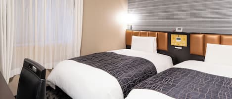 A hotel room with two beds, a desk, and a control panel on the wall.