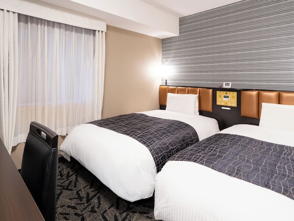 A hotel room with two beds, a desk, and a control panel on the wall.