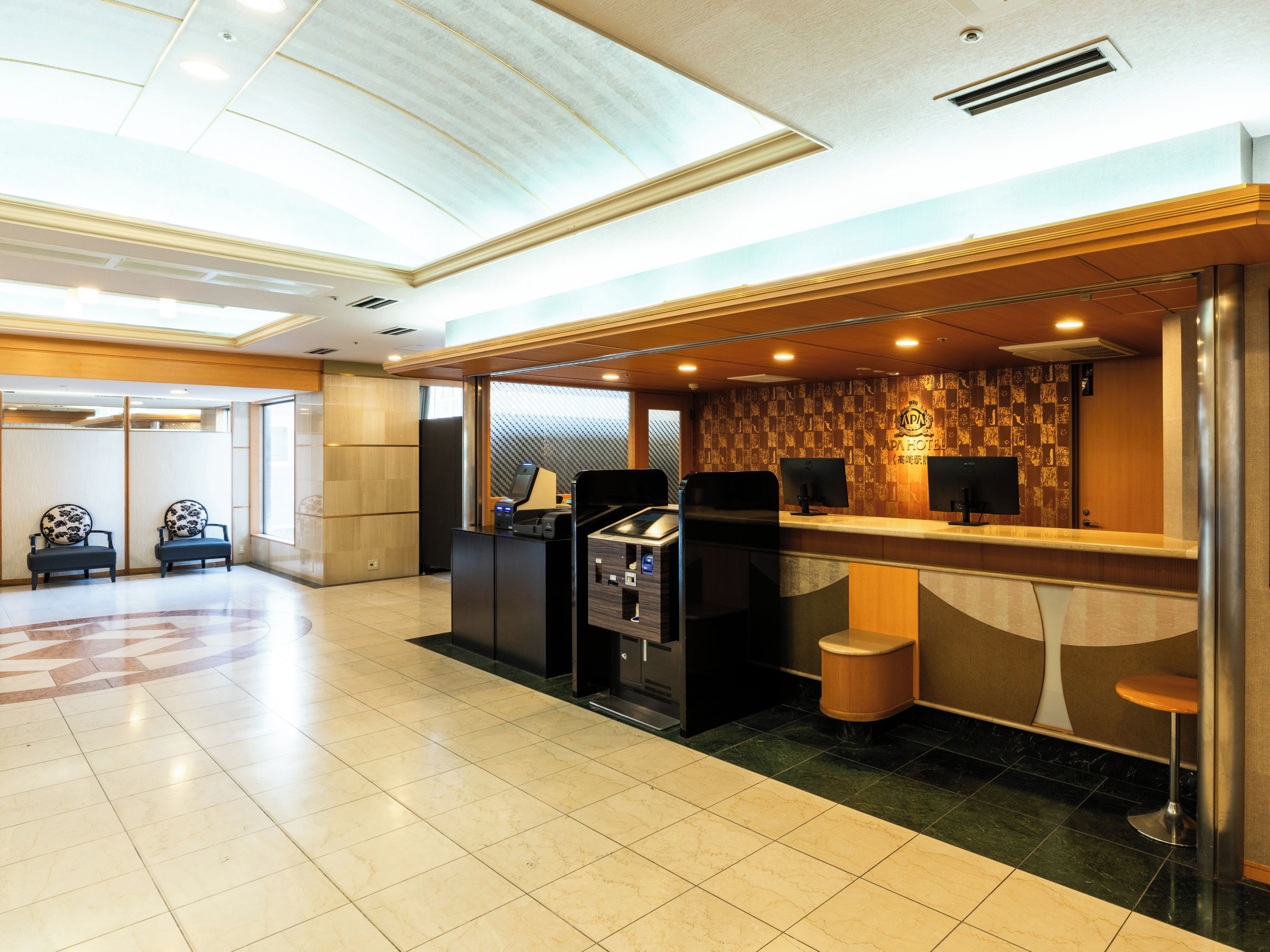 A hotel reception area with a check-in counter, seating area, and a self-service kiosk.