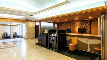 A hotel reception area with a check-in counter, seating area, and a self-service kiosk.