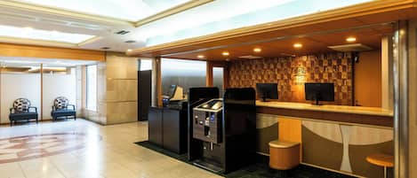 Zona de recepción de hotel con mostrador de registro, área de estar y quiosco de autoservicio.