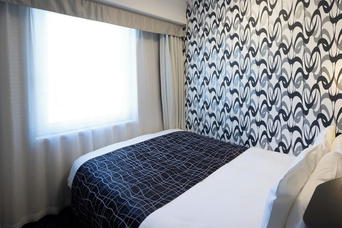 Ein Hotelzimmer mit Bett, Fenster mit Vorhängen und einer Wand mit Muster.