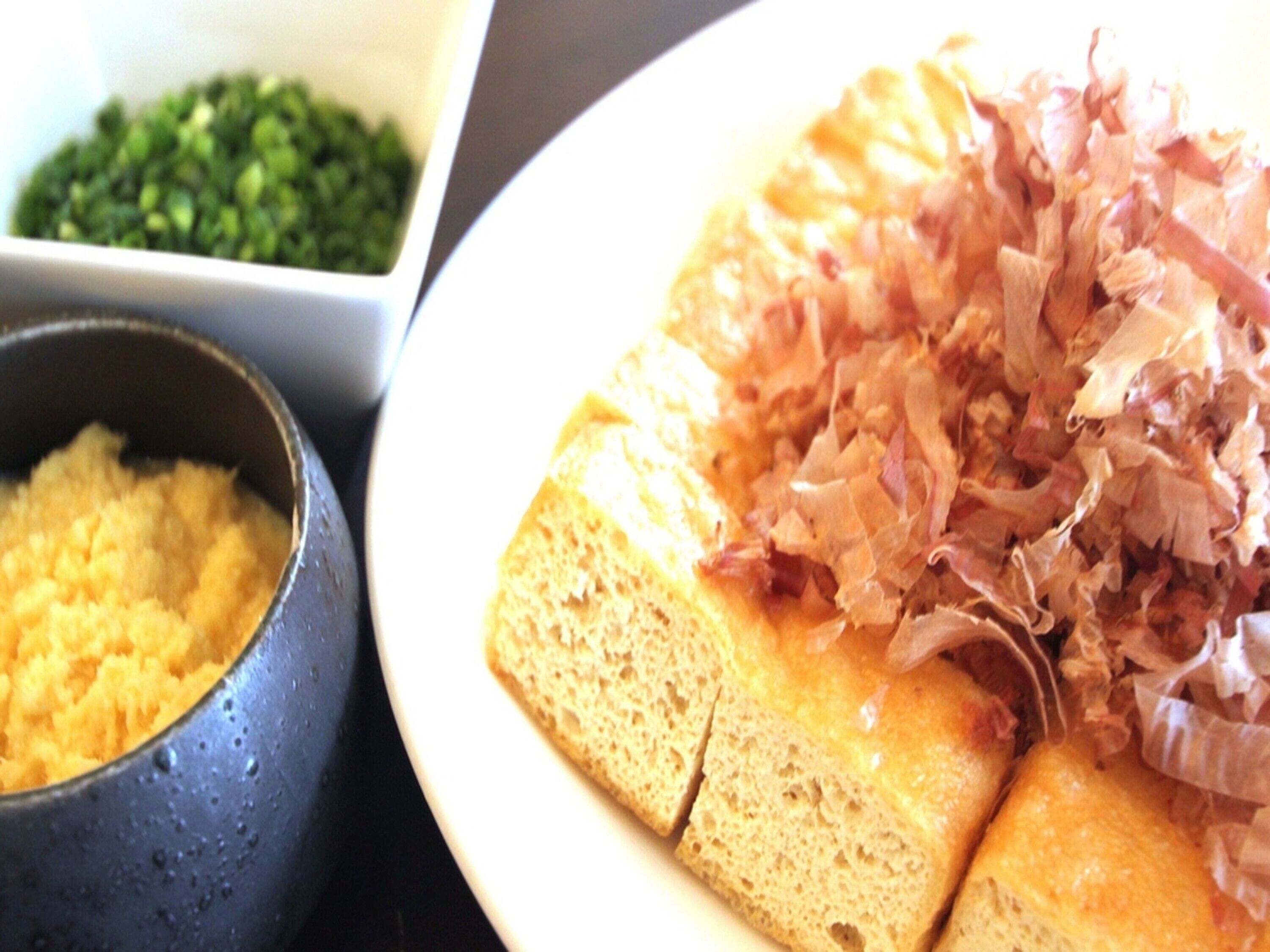Un plato de comida con una rebanada de pan cubierta de cebolla picada y un tazón de queso rallado.