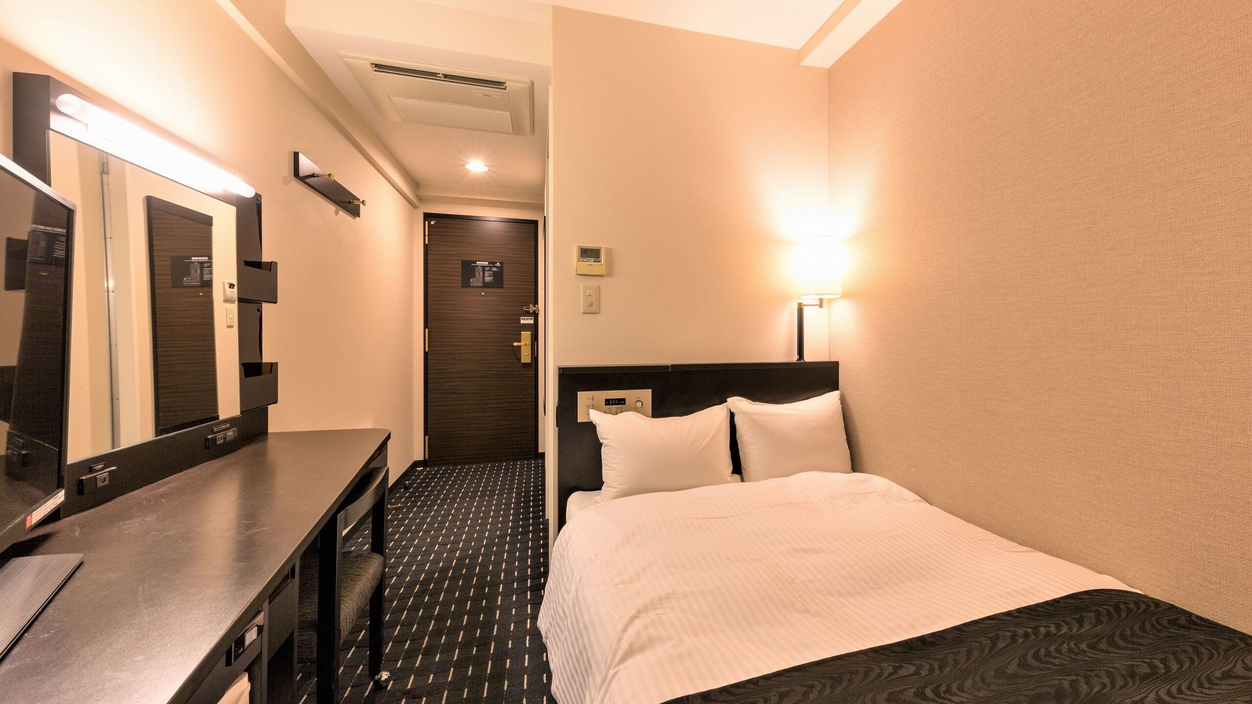 Ein Hotelzimmer mit Bett, Schreibtisch, Spiegel, Wanduhr und Tür.