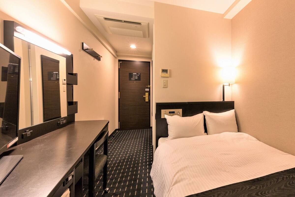 Ein Hotelzimmer mit Bett, Schreibtisch, Spiegel, Wanduhr und Tür.