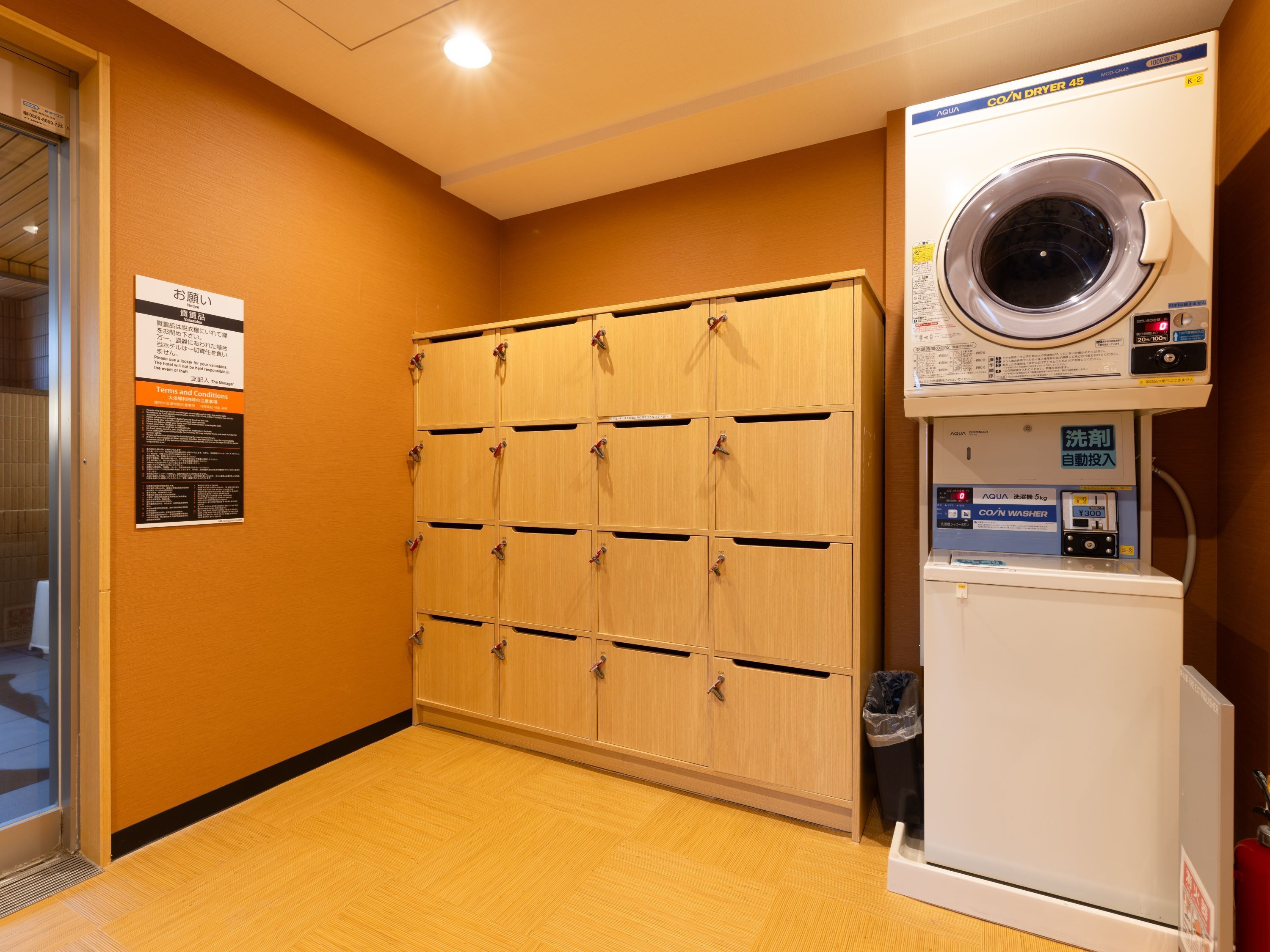 A laundry room with a washing machine and dryer, wooden lockers, and a sign with terms and conditions.