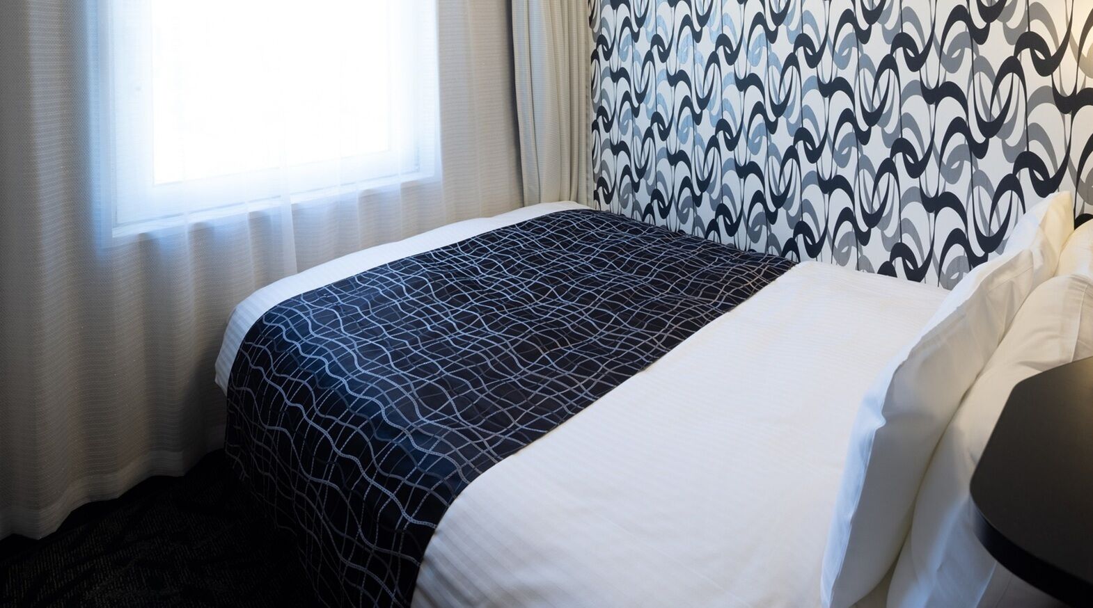 Een hotelkamer met een bed, een raam met gordijnen en een behang met patroon.
