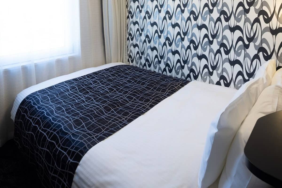 Una habitación de hotel con una cama, una ventana con cortinas y una pared con diseño.