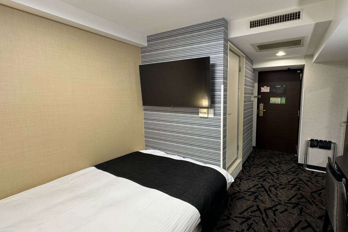 Una habitación de hotel con cama, televisor montado en la pared, puerta con un letrero y alfombra estampada.