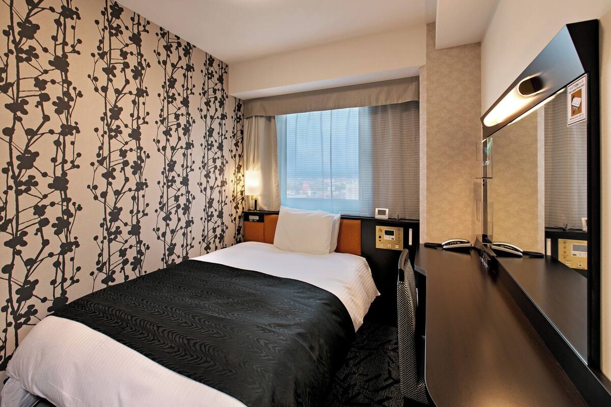 Habitación de hotel con cama, un espejo grande, una ventana con cortinas y una pared con estampado floral.
