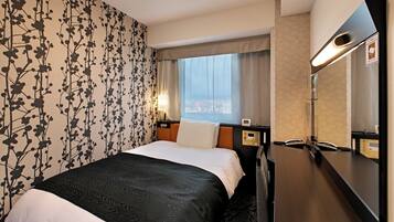 A hotel room with a bed, a large mirror, a window with curtains, and a wall with a floral pattern.