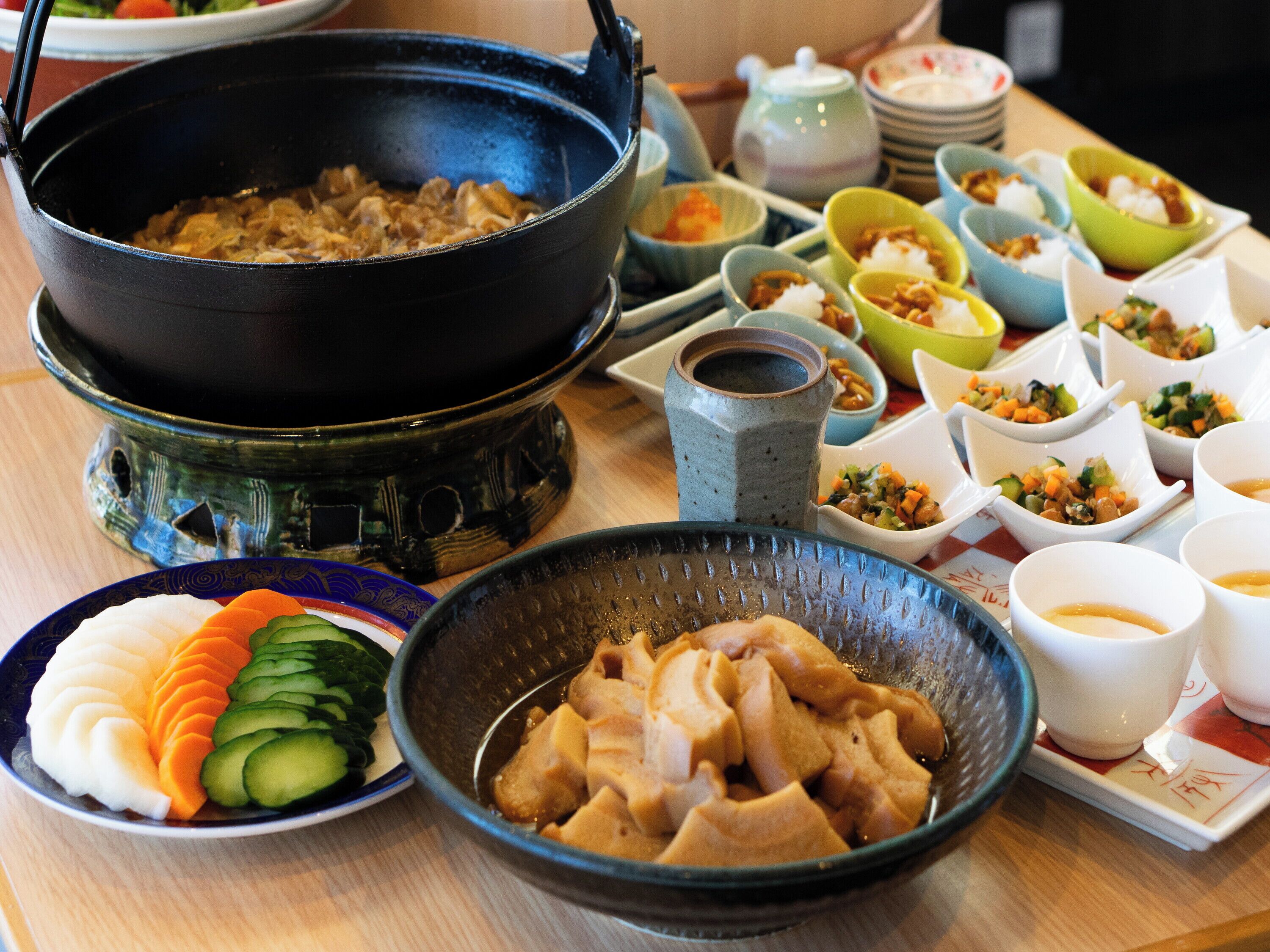 A table with various dishes, including a large pot, bowls of food, and a plate with sliced vegetables.