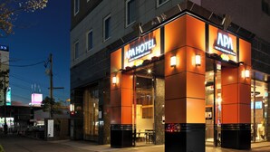 Un hôtel reconnaissable à son grand panneau « APA HOTEL », à ses larges fenêtres et à son entrée bien éclairée.