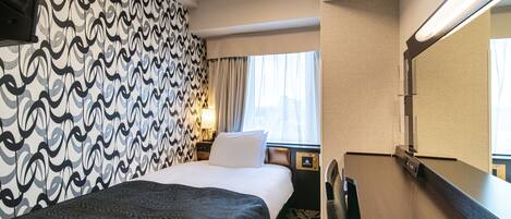 A hotel room with a patterned wallpaper, a bed with a dark cover, a nightstand with a lamp, and a large mirror.