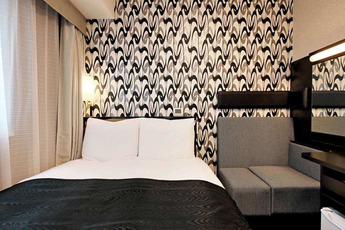Una habitación de hotel con una cama, un sofá y un papel tapiz estampado.