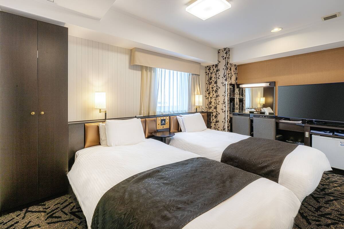 Habitación de hotel con dos camas, un escritorio, un televisor de pantalla plana, un espejo grande y una ventana con cortinas.