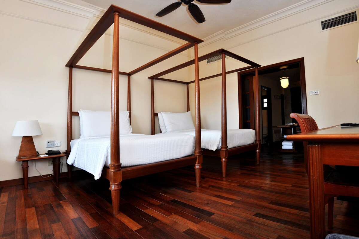 Una cama con dosel en una habitación de hotel con suelo de madera, un escritorio y una silla.