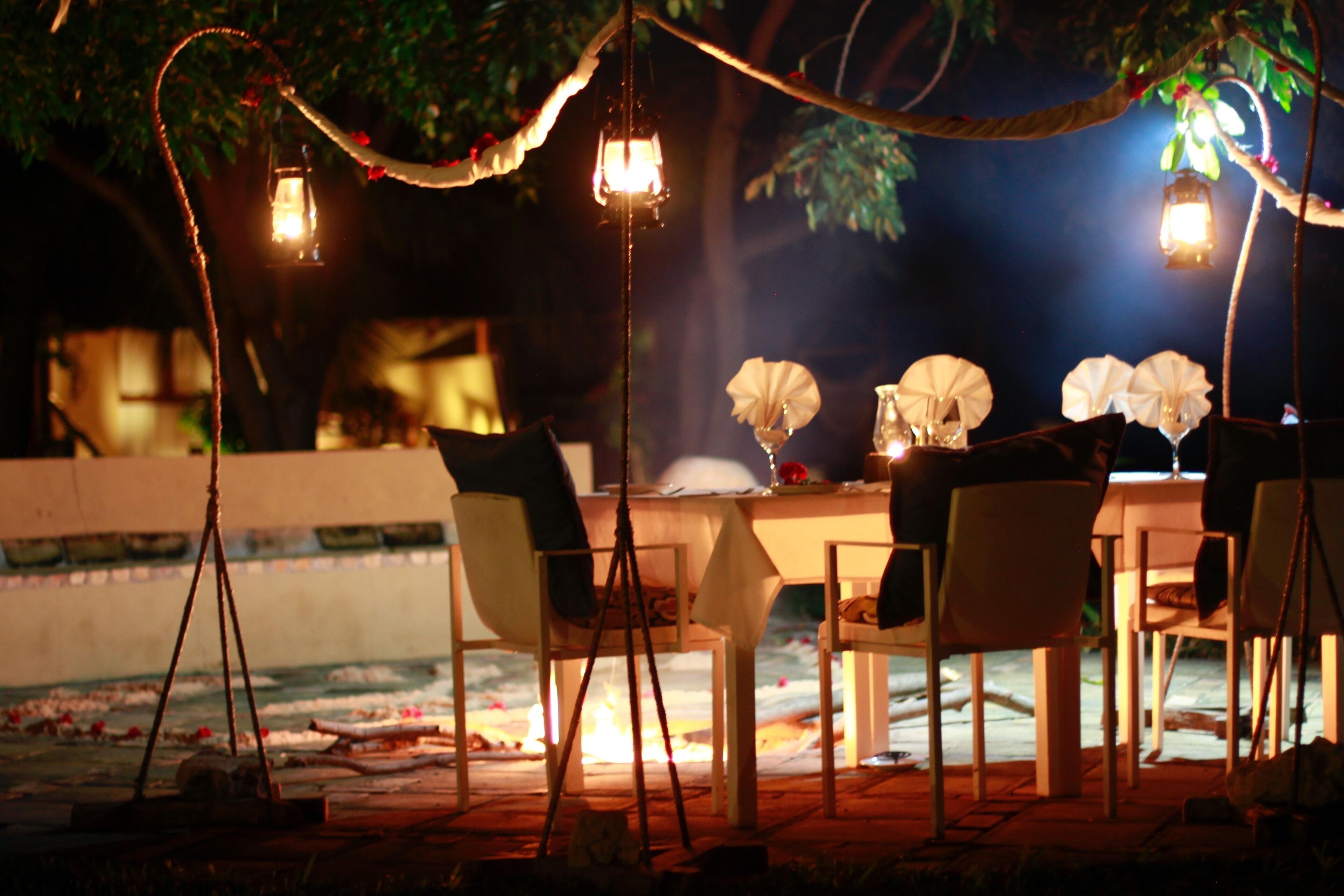 An outdoor dining area with tables and chairs, lanterns, and a water feature.