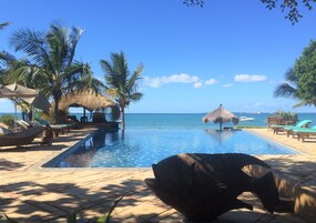A poolside area with lounge chairs, a thatched umbrella, and a view of the ocean.