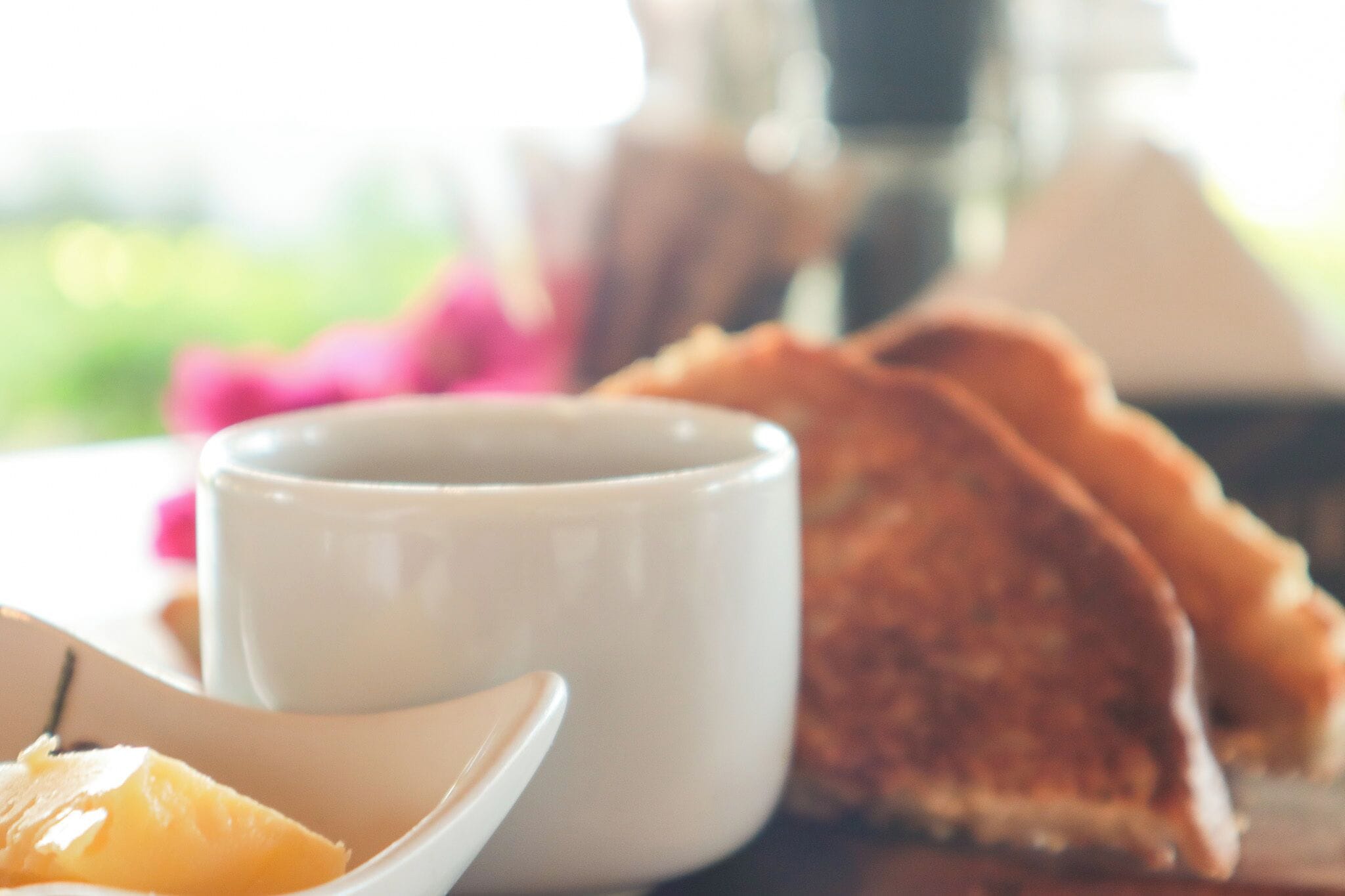 A white mug, a plate with a slice of orange, and a piece of bread on a table.