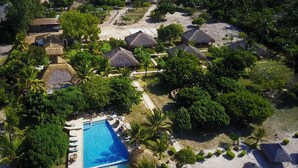 An aerial view of a resort with a swimming pool, thatched-roof structures, and lush greenery. - Villas do Indico Eco - Resort & Spa Lodge (Vilanculos)