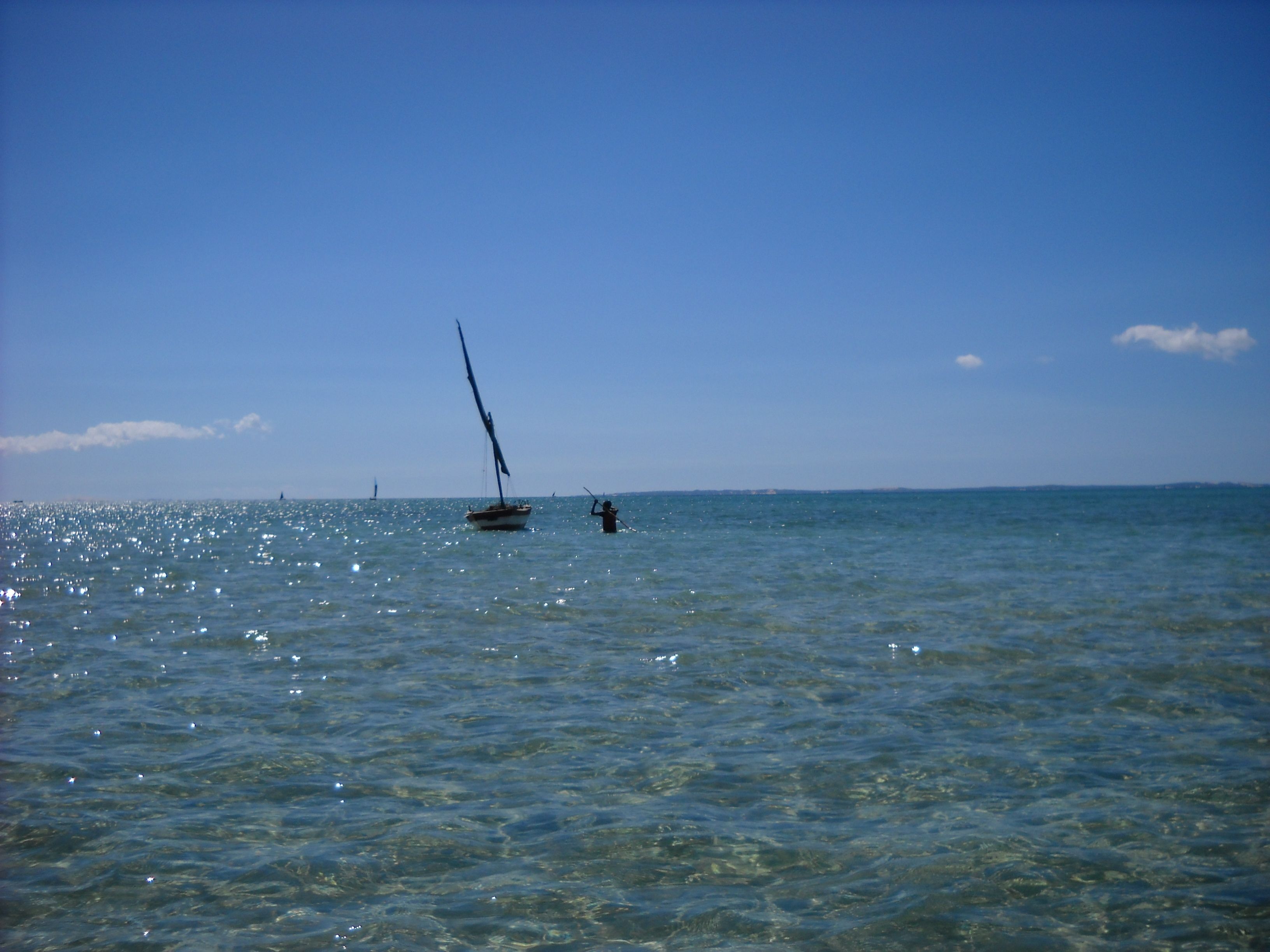 Klarer Blick auf das Meer mit einem Segelboot und einer Person im Wasser.