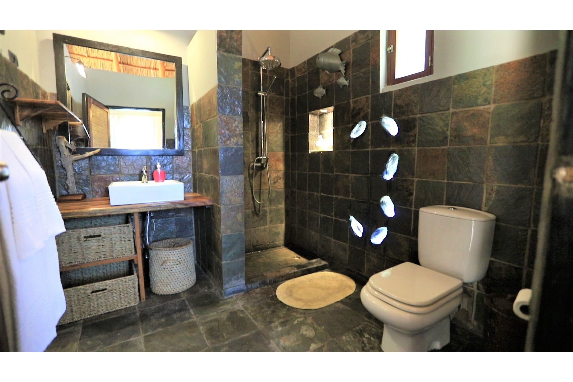 A bathroom with a stone wall, a white sink, a toilet, and a shower area.
