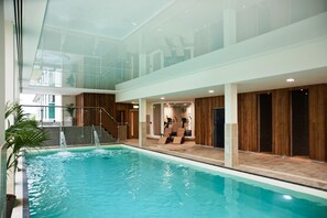 Una piscina interior con techo de vidrio, paredes de madera y equipo de ejercicios.