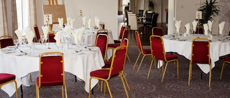 A dining area with tables set for six, each with red chairs and white tablecloths.
